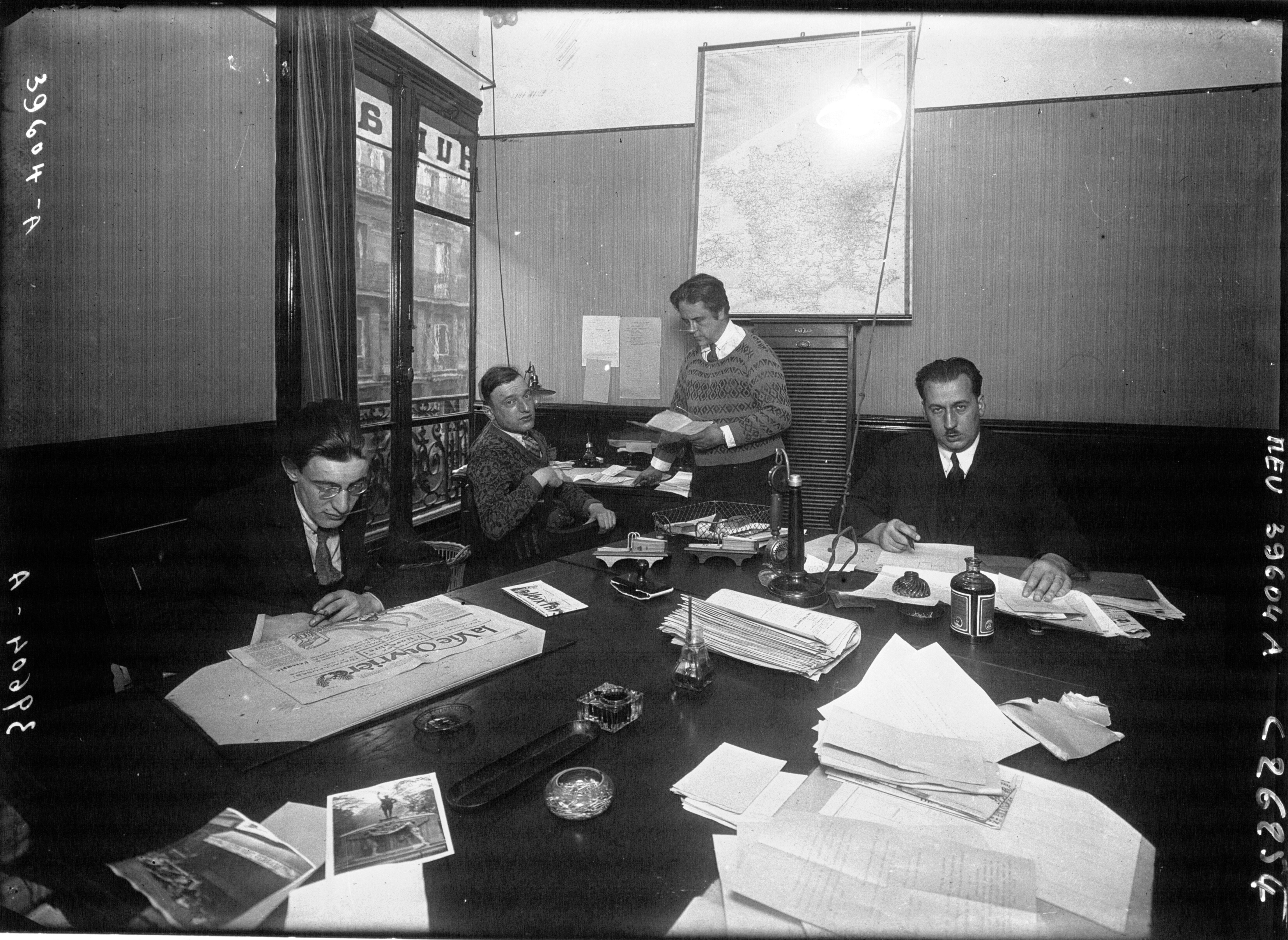 Salle de rédaction parisienne avec journalistes assis à des bureaux, photographiée en 1926.