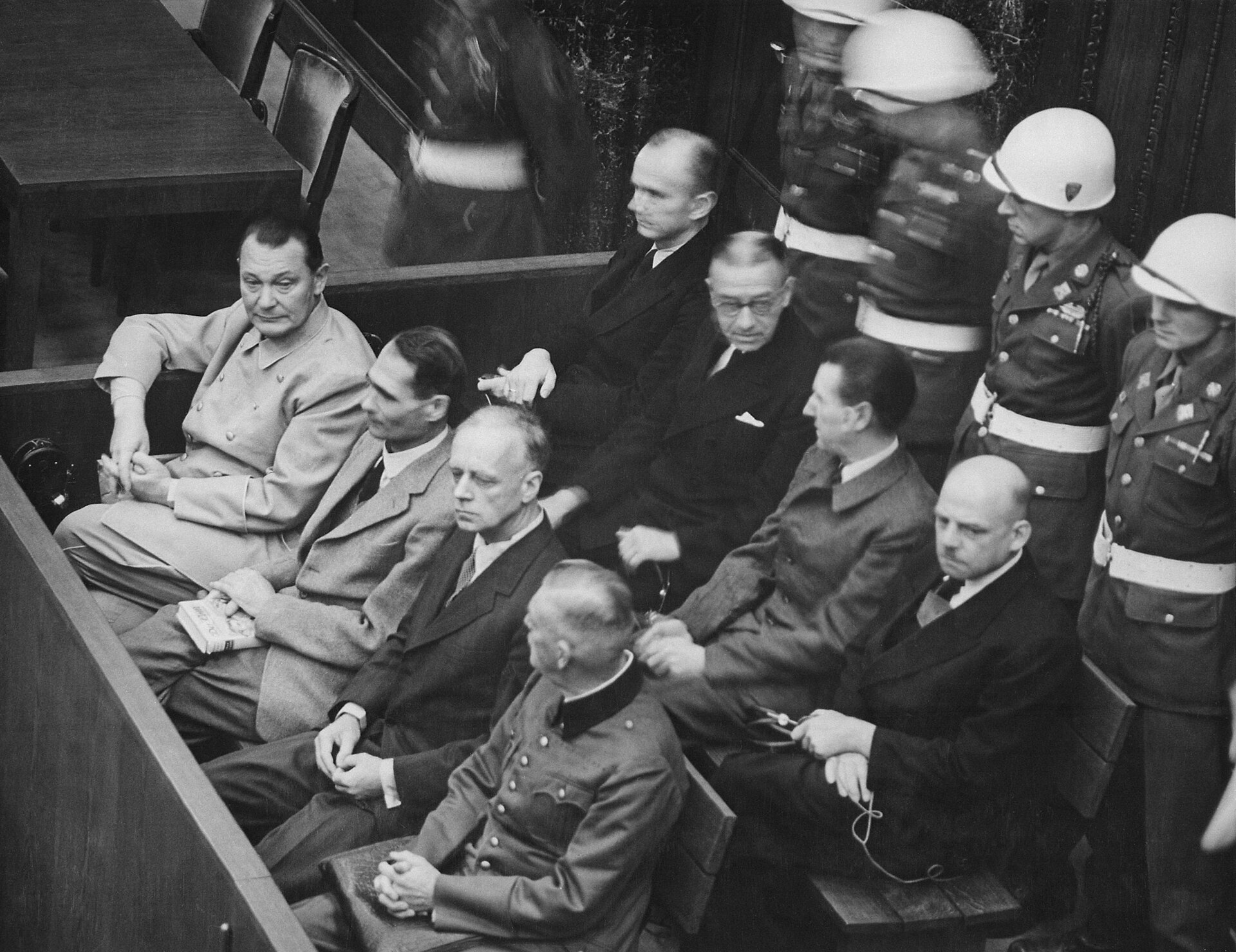 Photographie du procès de Nuremberg : accusés assis au banc, gardes derrière eux.